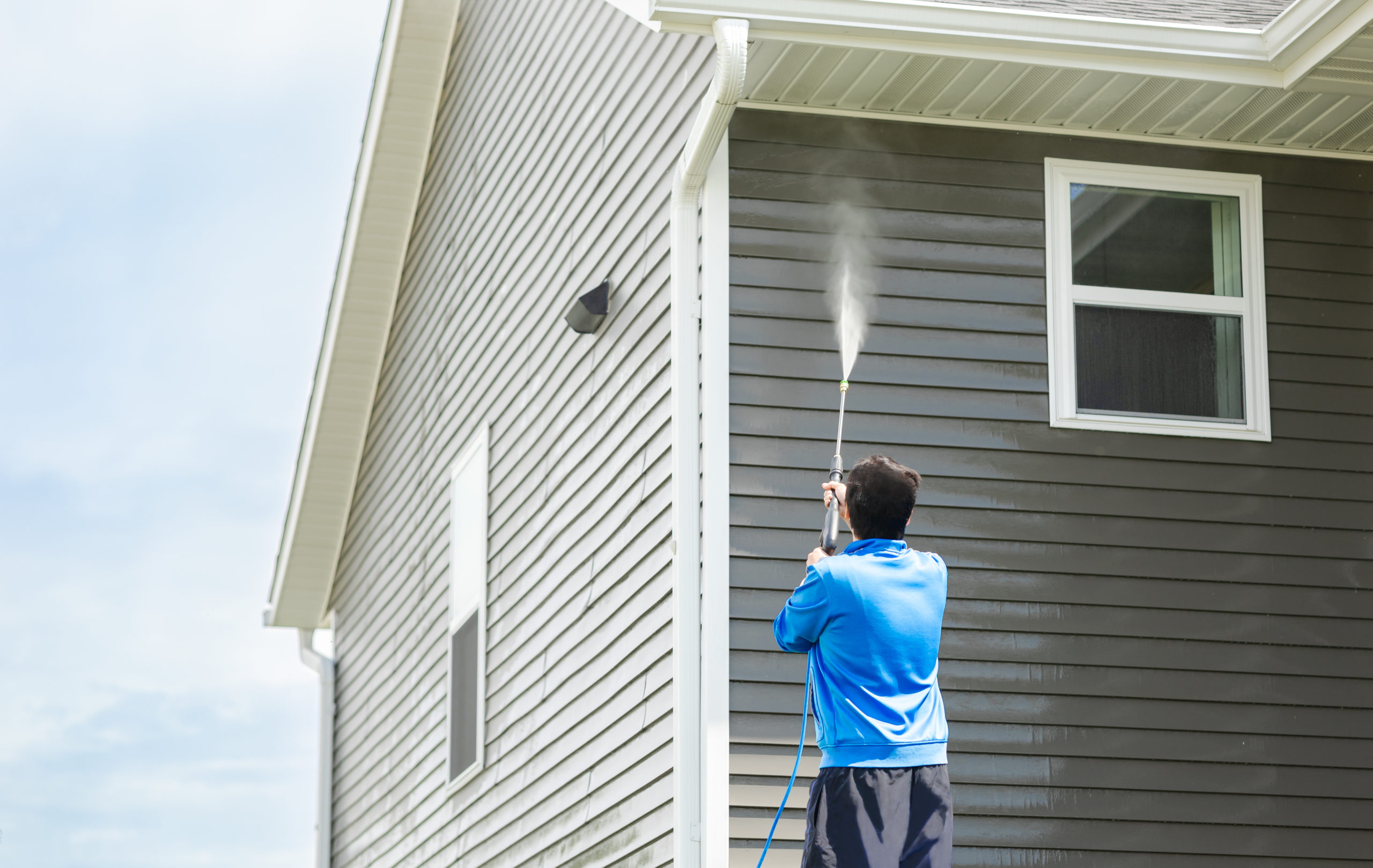 Man in blue jacket clean dusk and dirt from exterior siding and